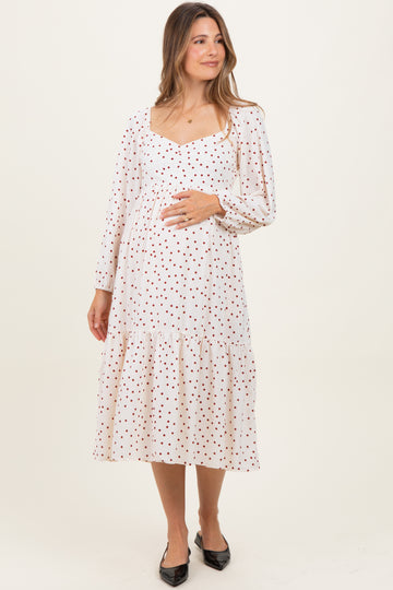 woman wearing a cream maternity dress with red polka dots and a tiered skirt, holding her baby bump