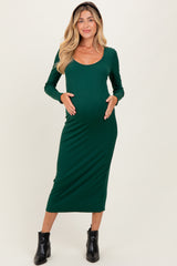 woman wearing a dark green long sleeve maternity dress with a scoop neckline and holding her baby bump