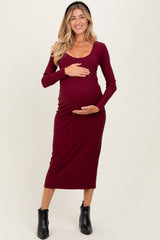 woman wearing a burgundy long sleeve maternity dress and holding her baby bump