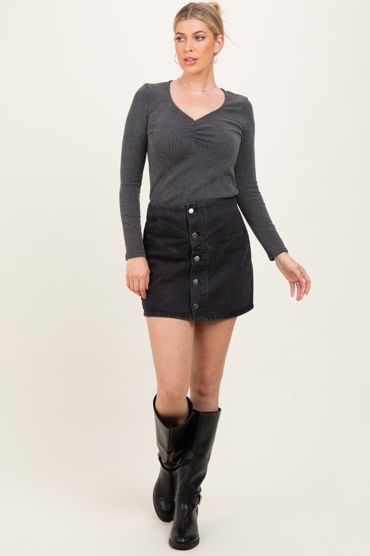 woman wearing a black ribbed long sleeve top and a black button-front mini skirt, paired with knee-high black boots
