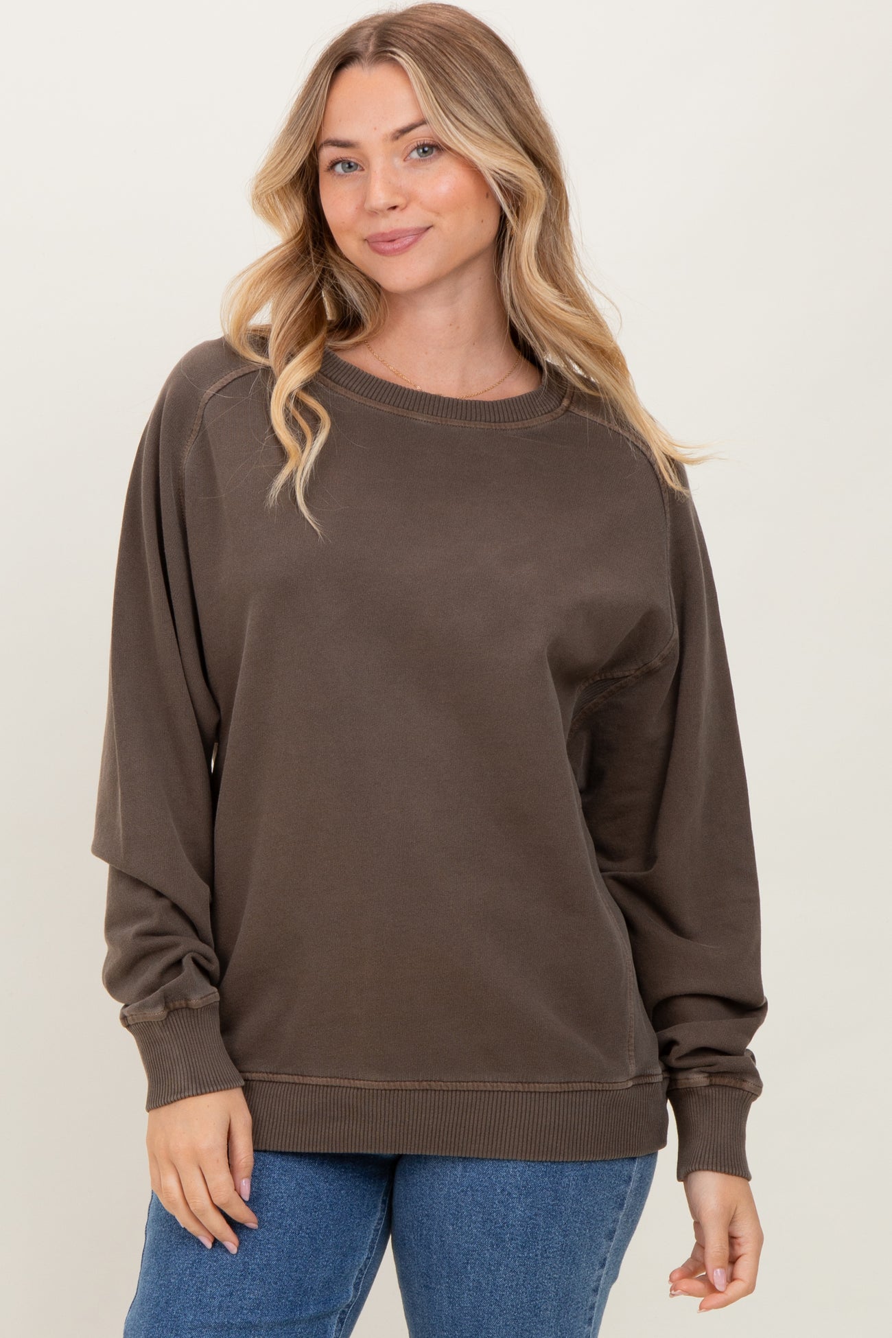 woman wearing a brown oversized sweatshirt with long sleeves and ribbed cuffs paired with blue jeans