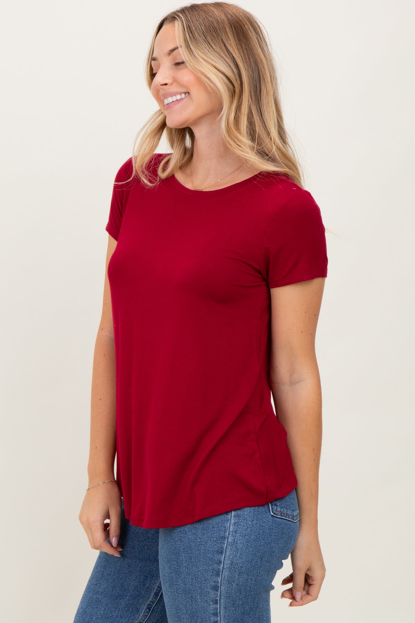 woman wearing a fitted burgundy short sleeve top paired with jeans, smiling against a light background