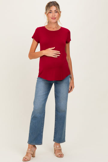 woman wearing a burgundy short sleeve maternity top and blue flared jeans, holding her baby bump