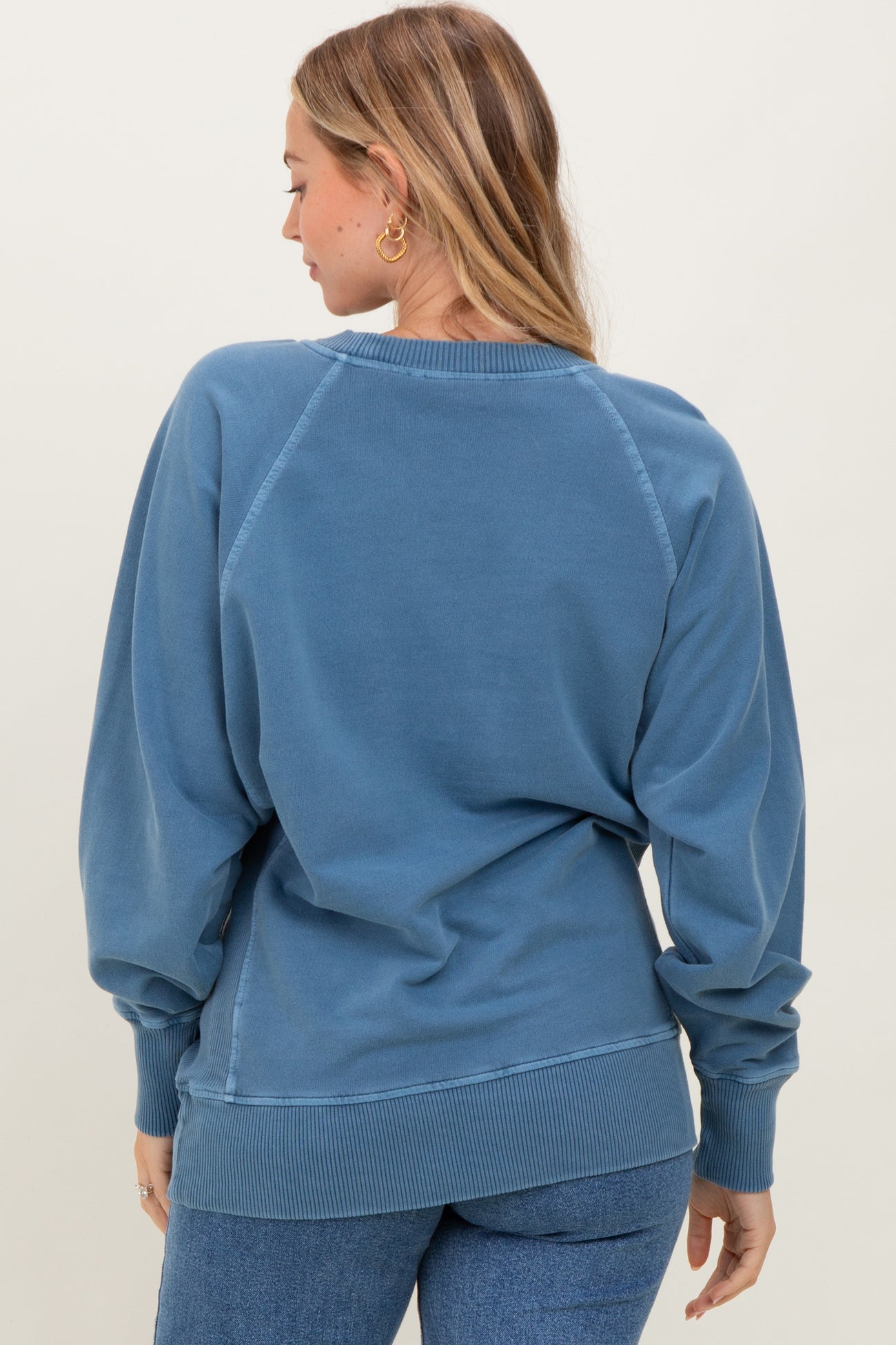 woman wearing a blue oversized sweatshirt with balloon sleeves and ribbed hem, viewed from the back