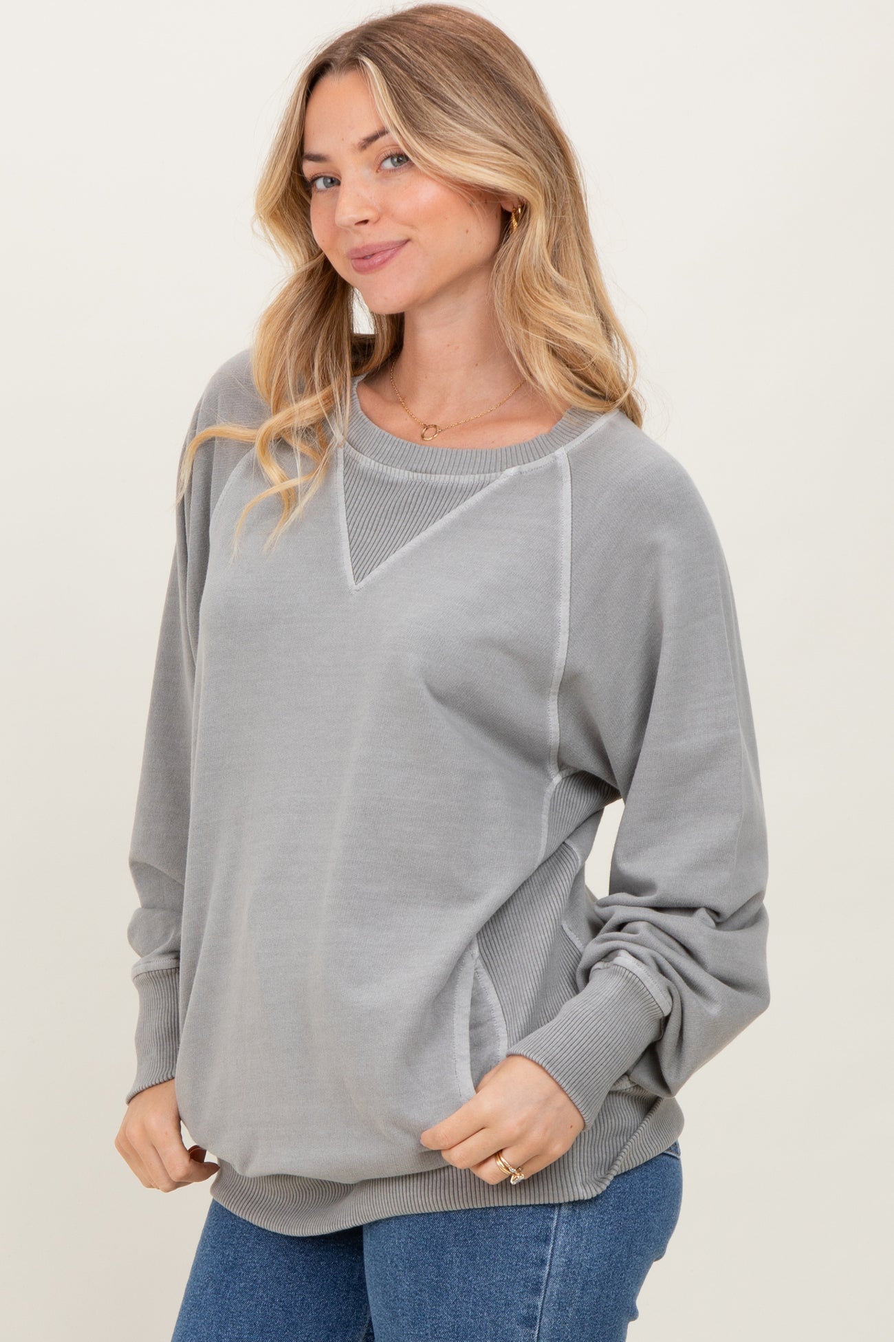 woman wearing a gray oversized sweatshirt with a v-neck and long sleeves, paired with blue jeans