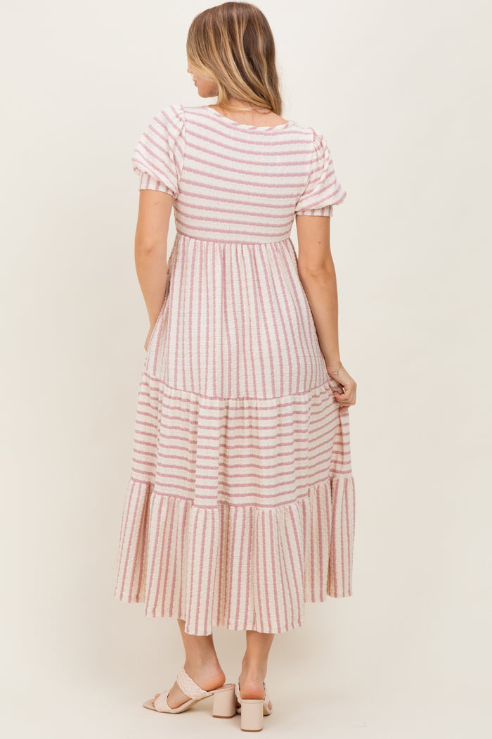 woman wearing a pink and white striped tiered maxi dress, showing the back view and short puff sleeves