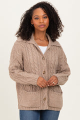 woman wearing a beige cable knit cardigan with a collar and pockets, paired with a white top and blue jeans