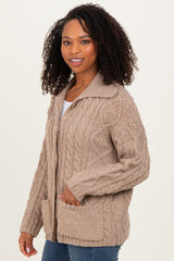 woman wearing a light brown cable knit cardigan with a collar and front pockets, smiling at the camera