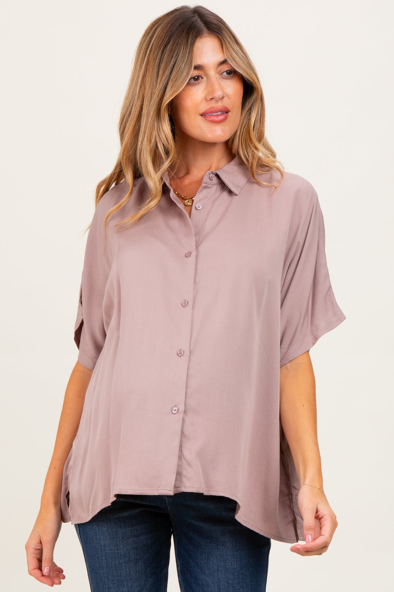 woman wearing a dusty rose short sleeve button-up maternity shirt with a relaxed fit and curved hem