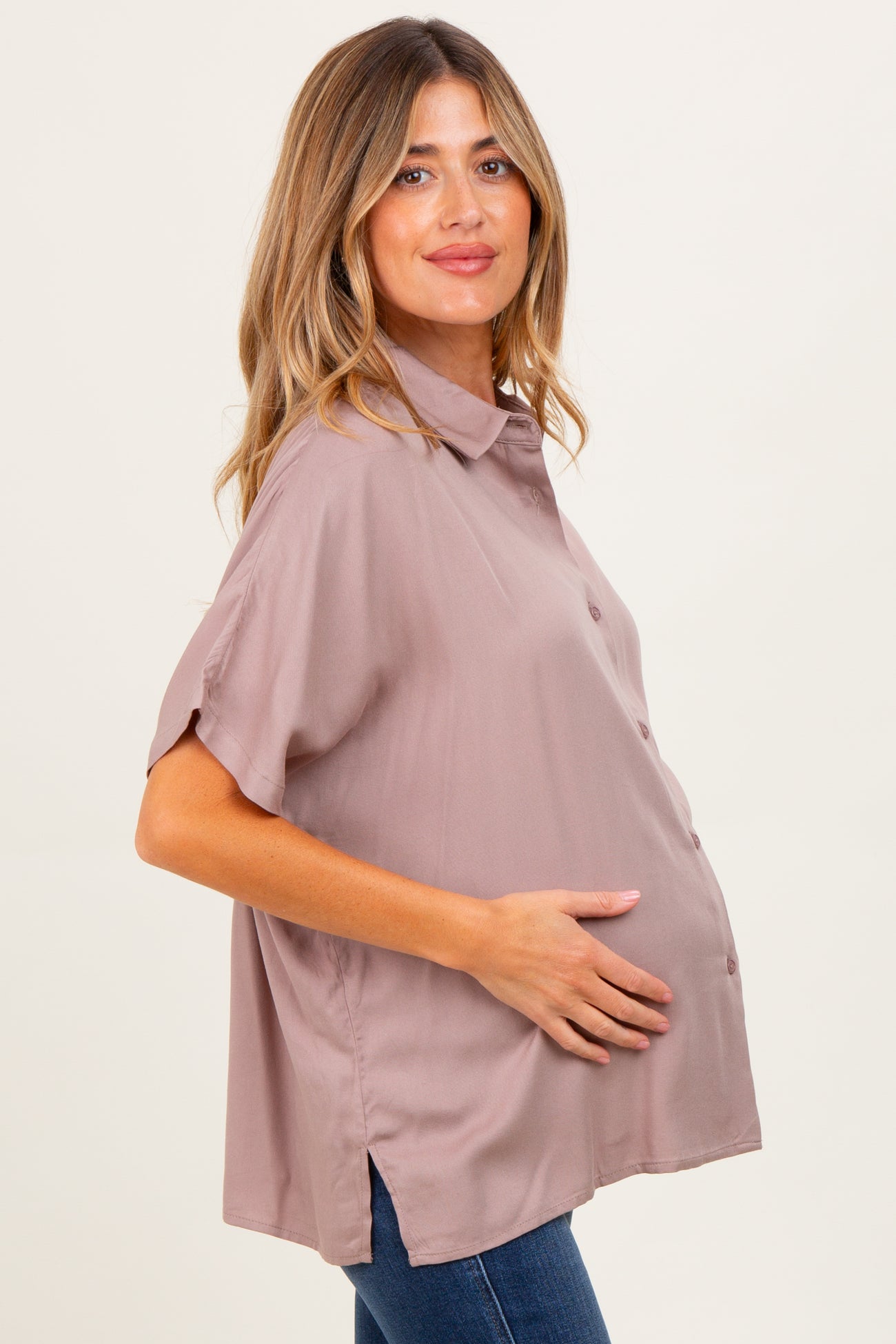 woman wearing a mauve short sleeve maternity button-up blouse and holding her baby bump