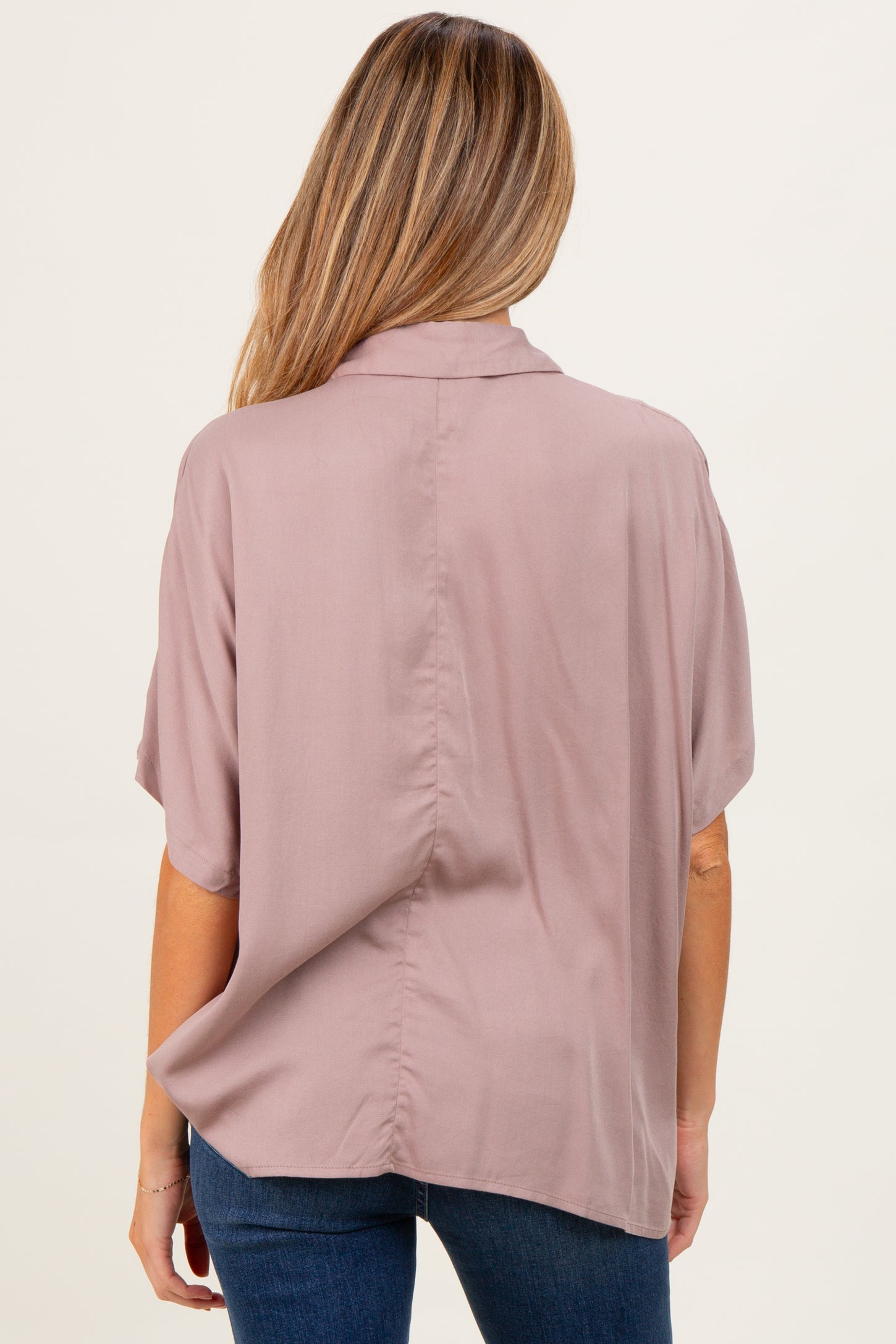 woman wearing a light mauve short sleeve maternity top, seen from the back, paired with dark jeans