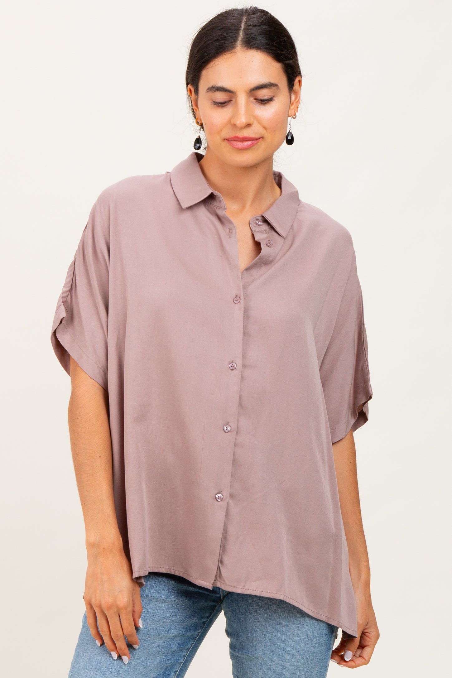 woman wearing a mauve oversized button-up shirt with short sleeves and relaxed fit, paired with blue jeans