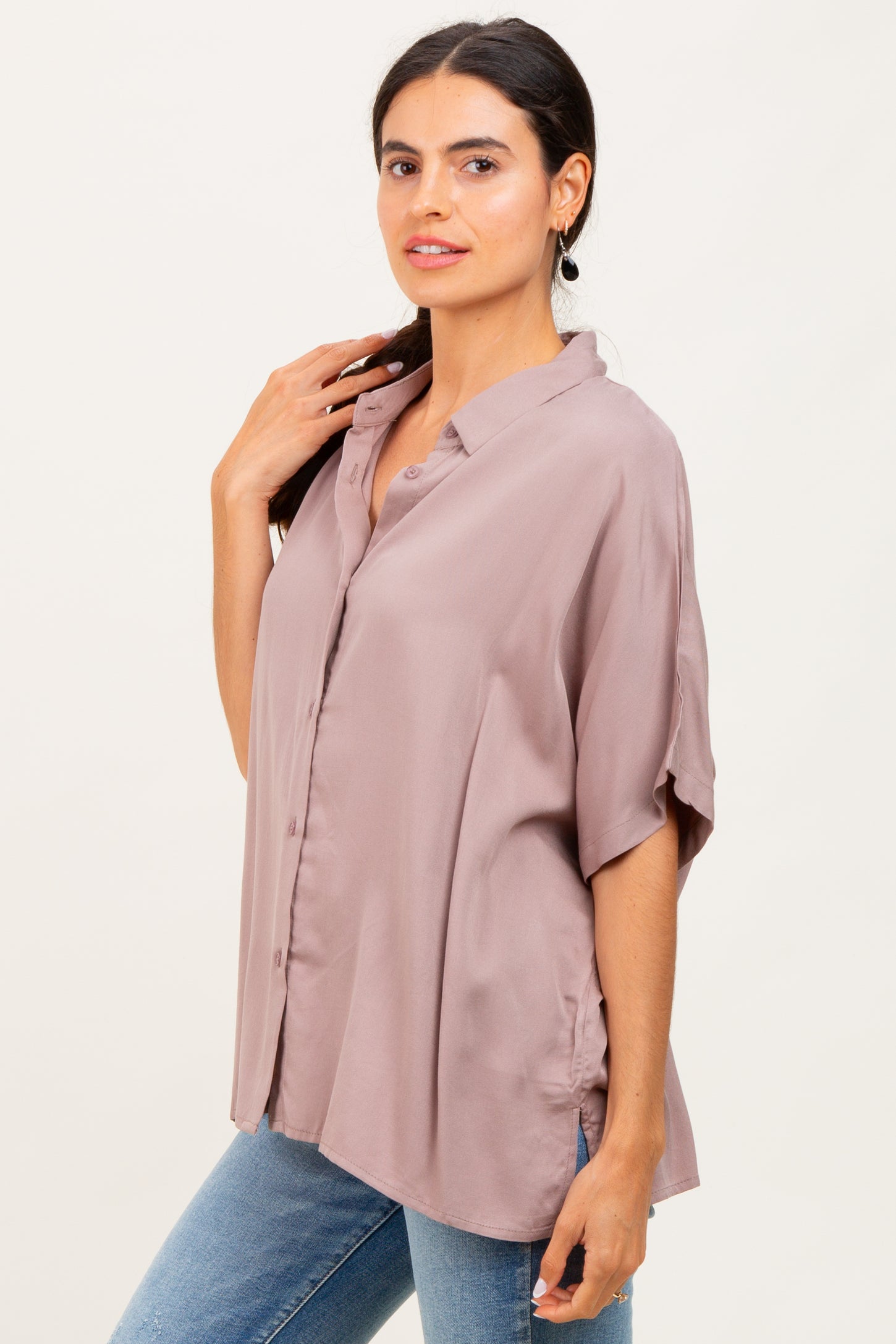 woman wearing a light mauve oversized button-up shirt with rolled sleeves and a relaxed fit paired with blue jeans