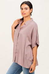 woman wearing a light mauve oversized button-up shirt with rolled sleeves and a relaxed fit paired with blue jeans