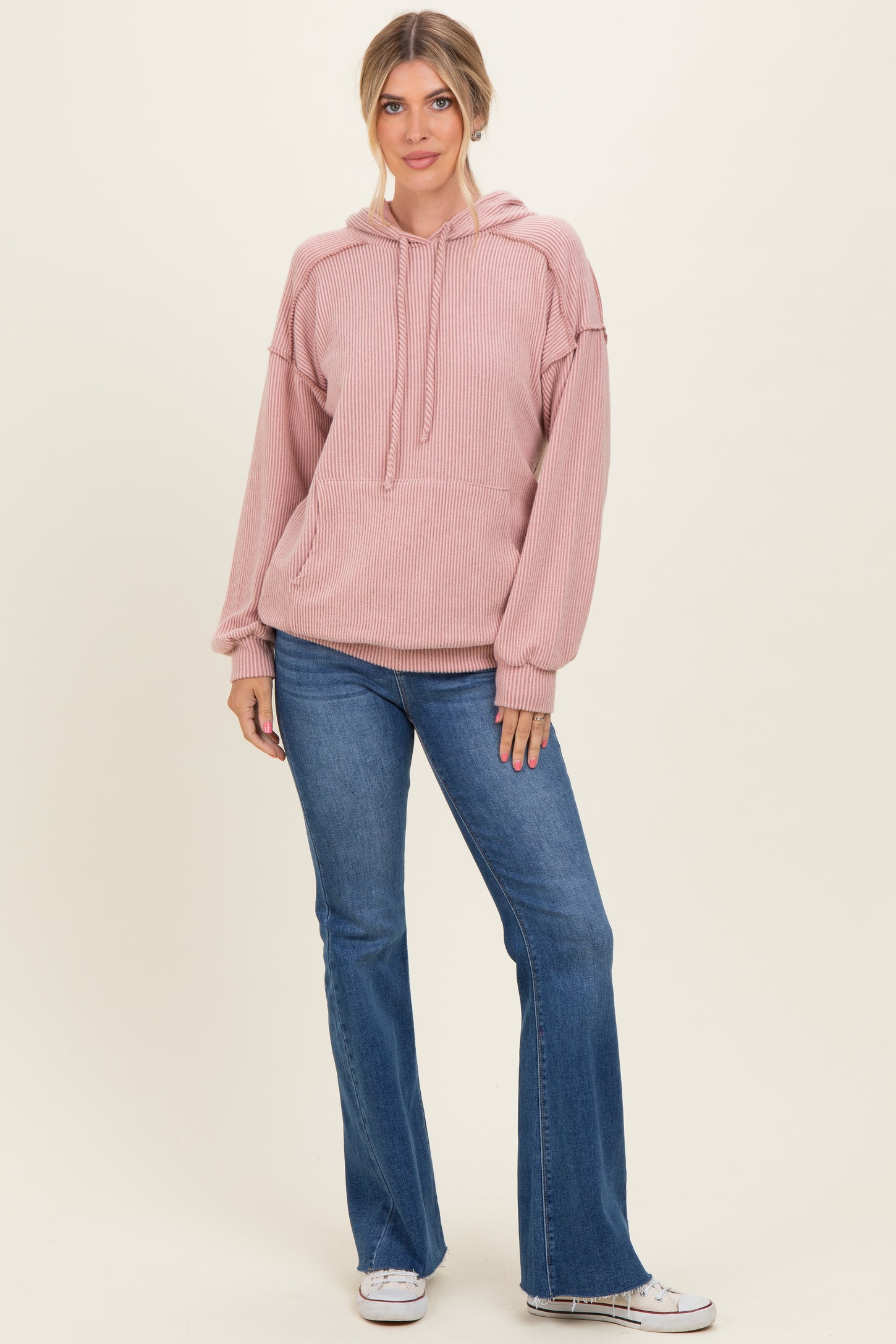 woman wearing a light pink ribbed hoodie with a front pocket and relaxed sleeves, paired with flare jeans