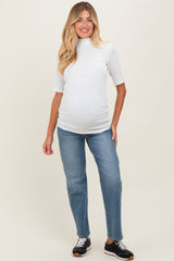 woman wearing a white ribbed maternity top and blue jeans, showing her baby bump