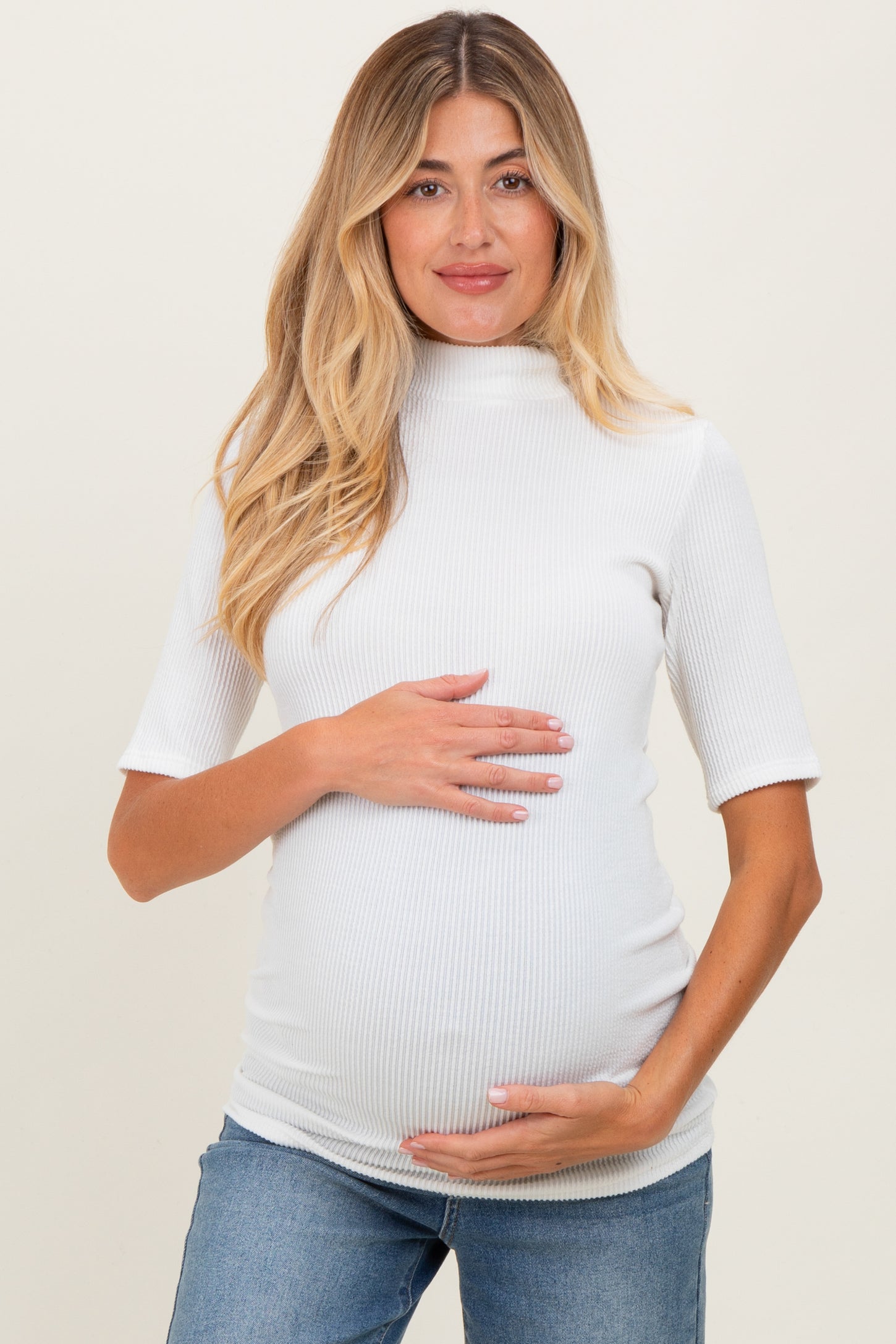woman wearing a white ribbed short sleeve maternity top and holding her baby bump