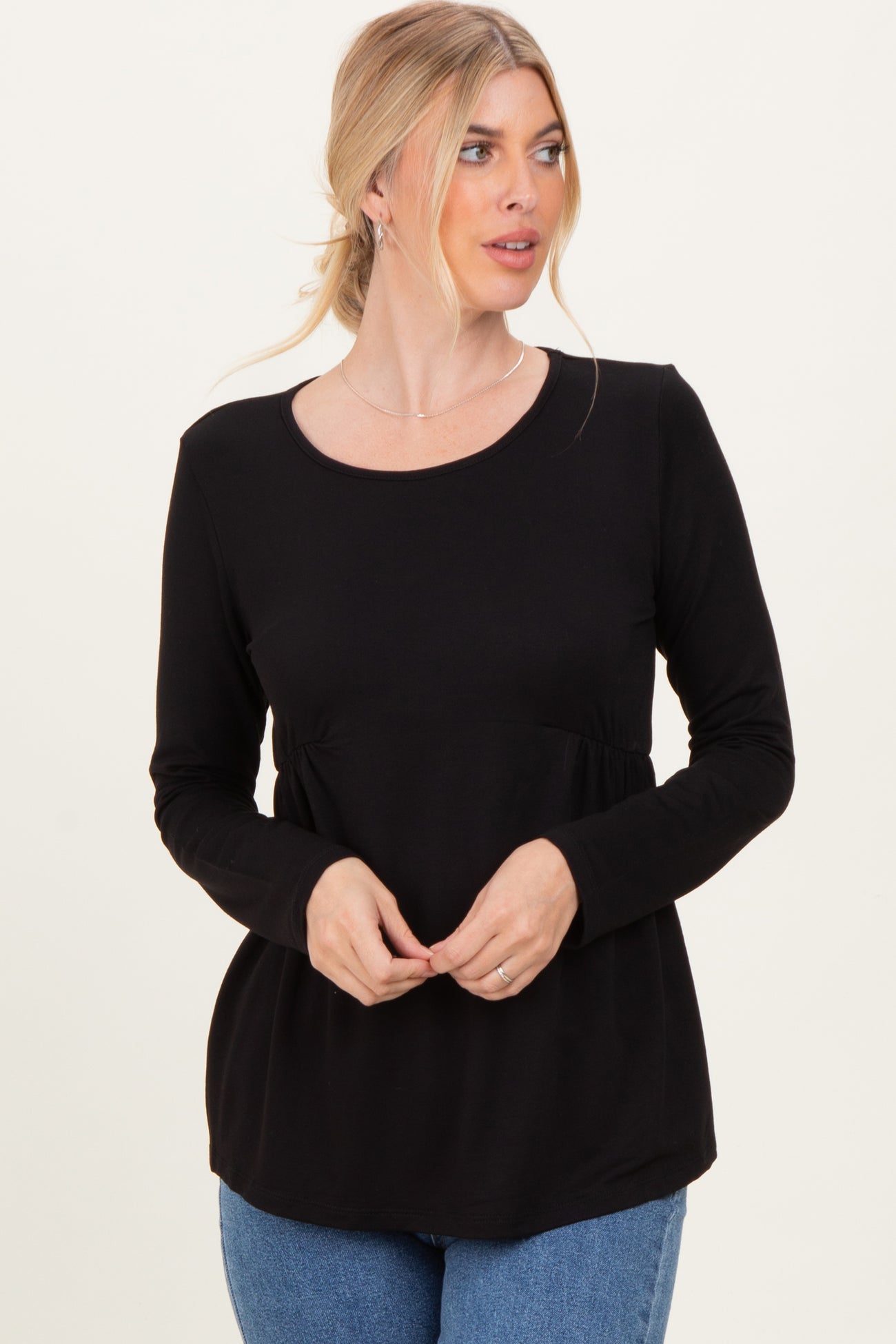 woman wearing a black long sleeve top with a fitted waist and relaxed fit, standing and looking to the side