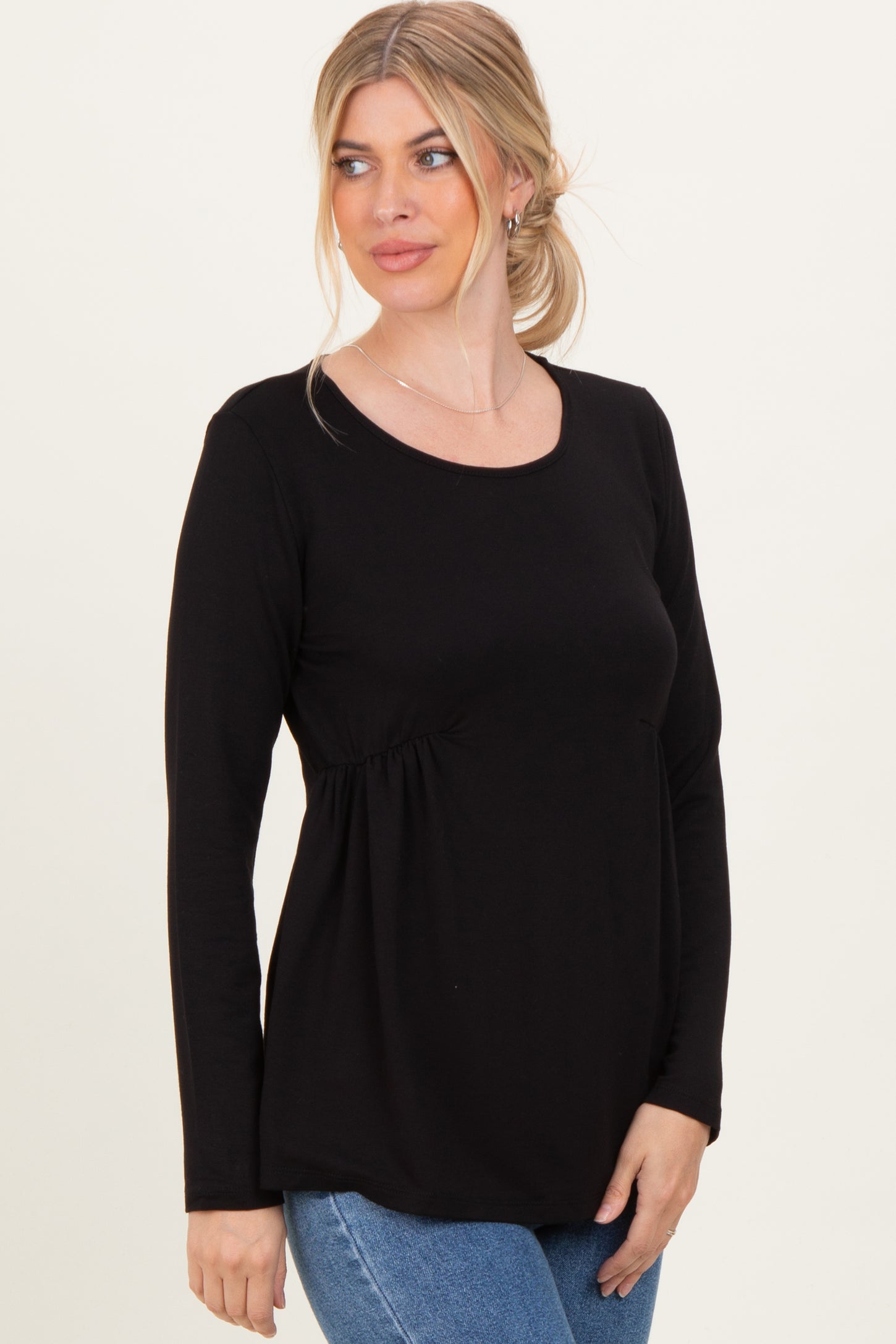 woman wearing a black long sleeve top with gathered detailing at the waist and styled with blue jeans
