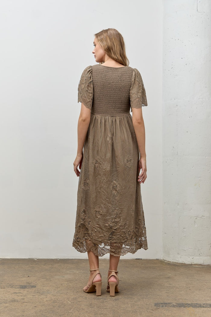 woman wearing a taupe embroidered midi dress with short sleeves and a smocked bodice, showing the back view
