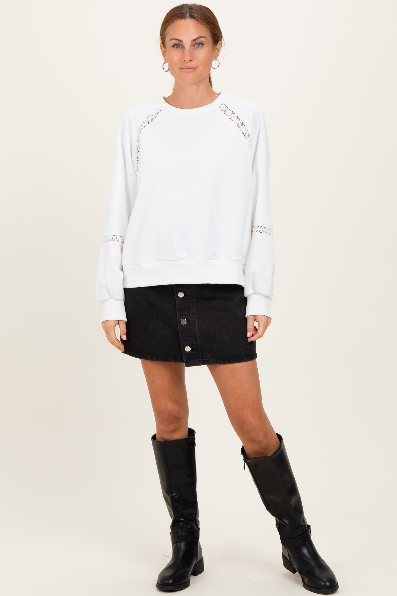 woman wearing a white sweatshirt with lace details and a black denim skirt, paired with knee-high black boots