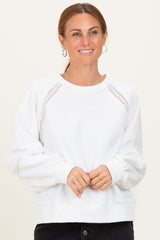 woman wearing a white sweatshirt with lace detail and puff sleeves, smiling against a neutral background