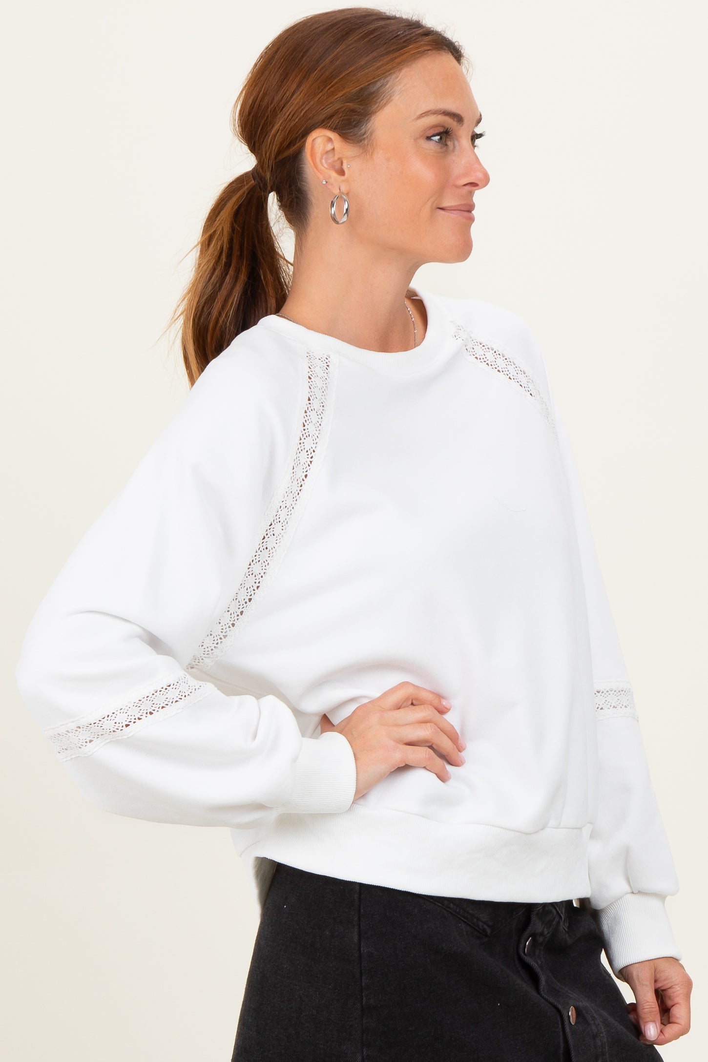 woman wearing a white sweatshirt with lace details on the sleeves and a relaxed fit