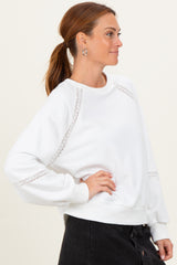 woman wearing a white sweatshirt with lace details on the sleeves and a relaxed fit