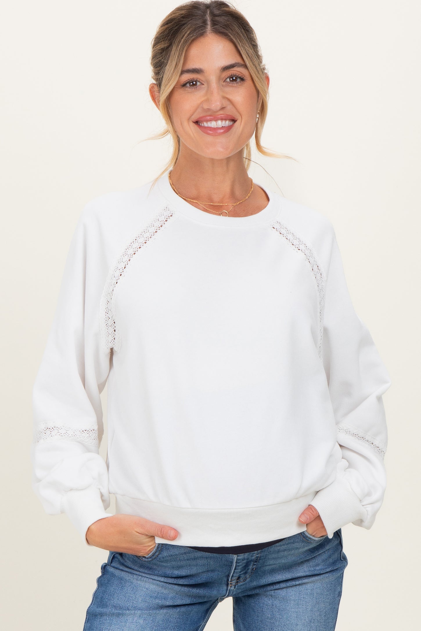 woman wearing a white maternity sweatshirt with lace details and relaxed fit, smiling with hands in pockets
