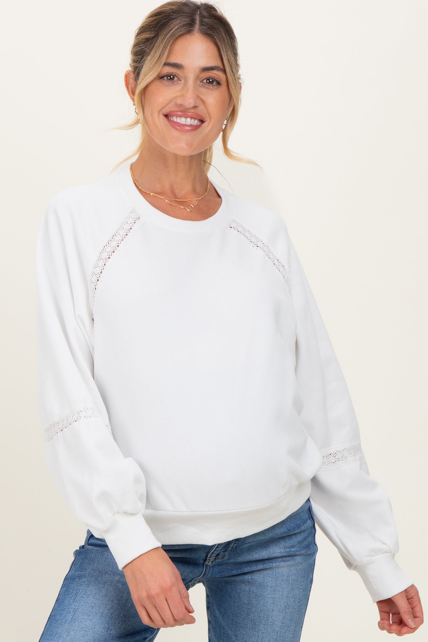woman wearing a white maternity sweatshirt with lace detail and balloon sleeves, paired with blue jeans