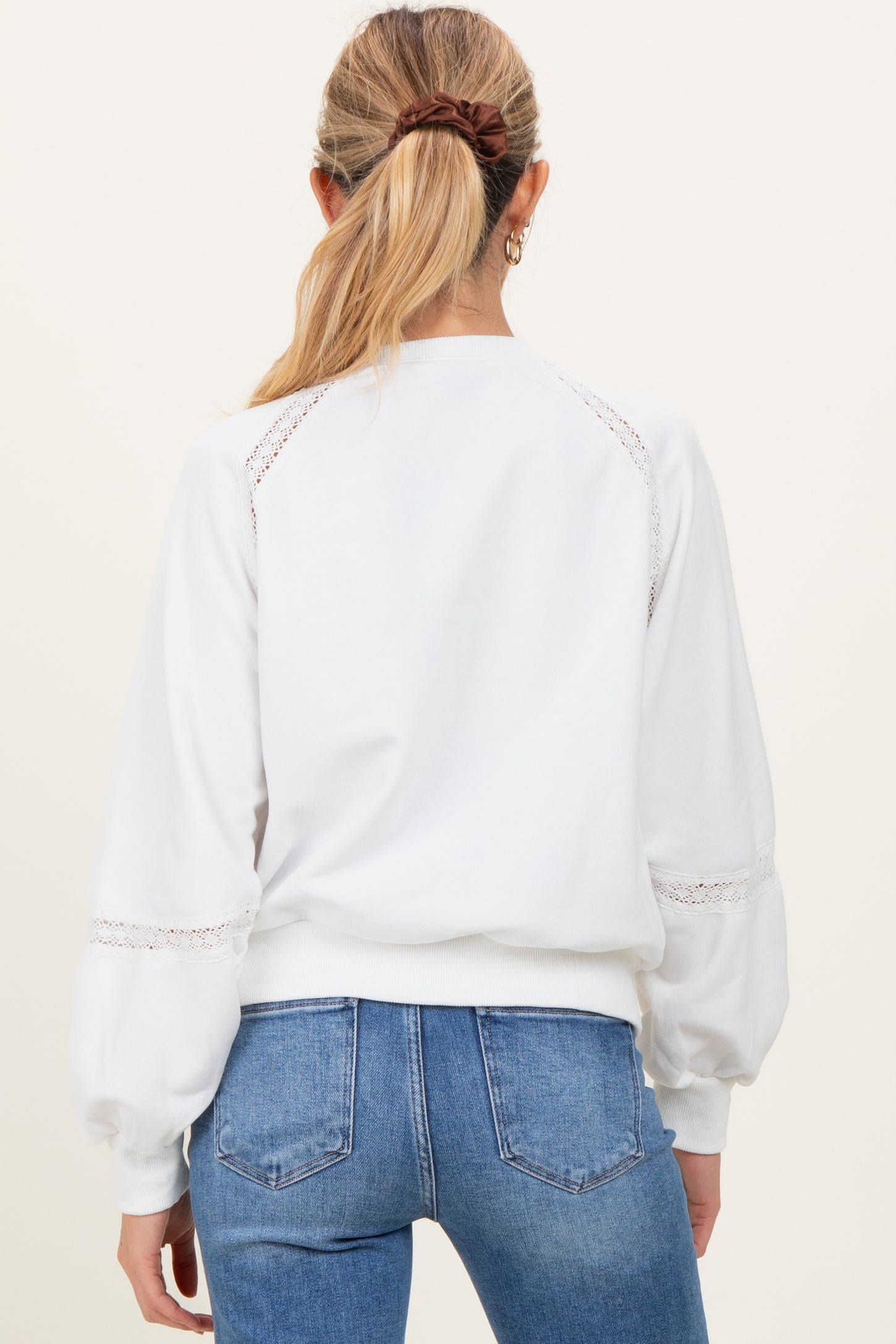 woman wearing a white maternity sweatshirt with lace detail on sleeves, styled with high-waisted jeans