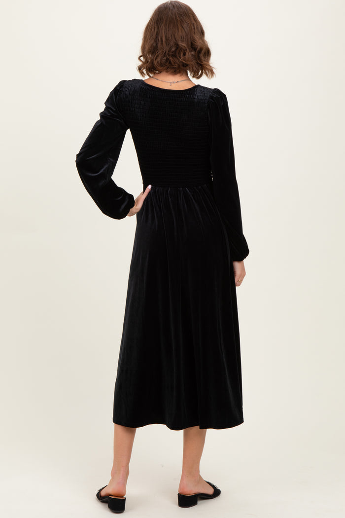 woman wearing a black velvet midi dress with a smocked back and long sleeves, viewed from the back
