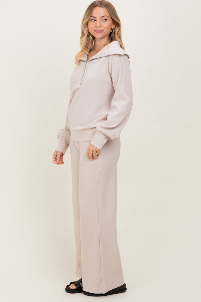 woman wearing a light beige hooded pullover and matching wide leg pants, standing in profile against a plain background
