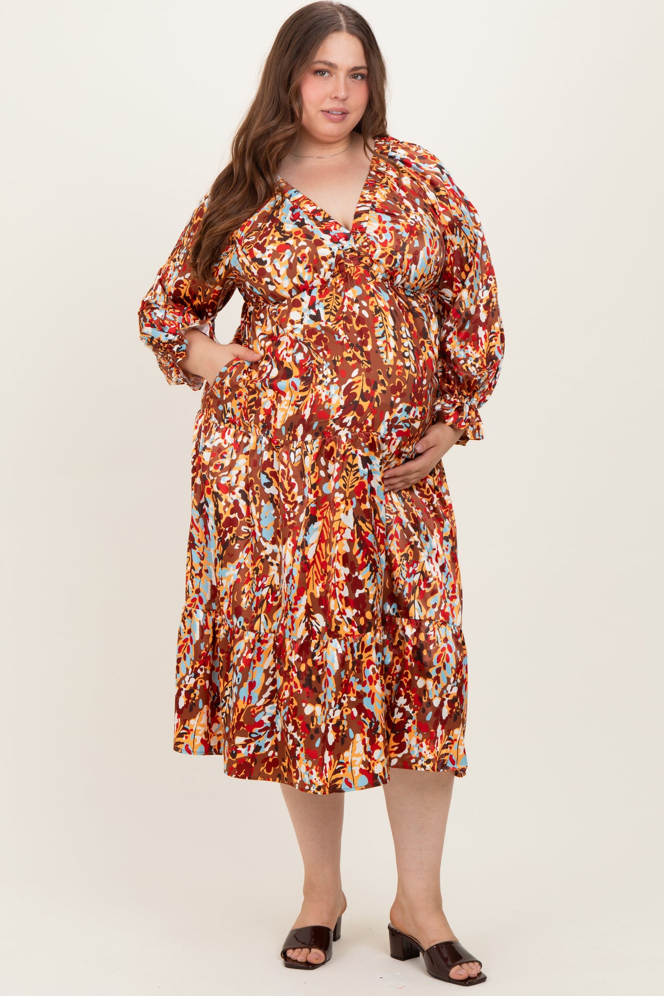 woman wearing a floral print maternity plus dress with a wrap style and puff sleeves, holding her baby bump