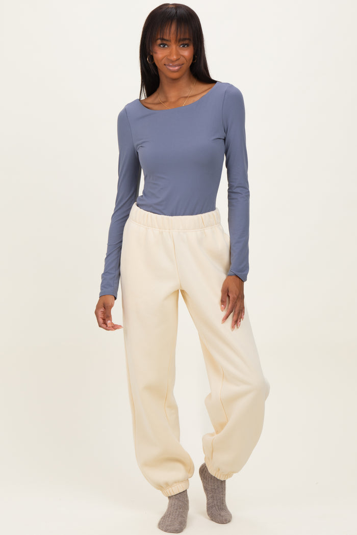 woman wearing a long sleeve blue top and cream-colored tapered sweatpants with cuffs at the ankles