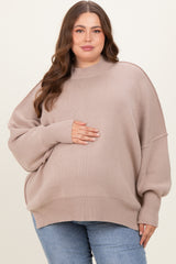 woman wearing a light beige oversized maternity sweater and holding her baby bump