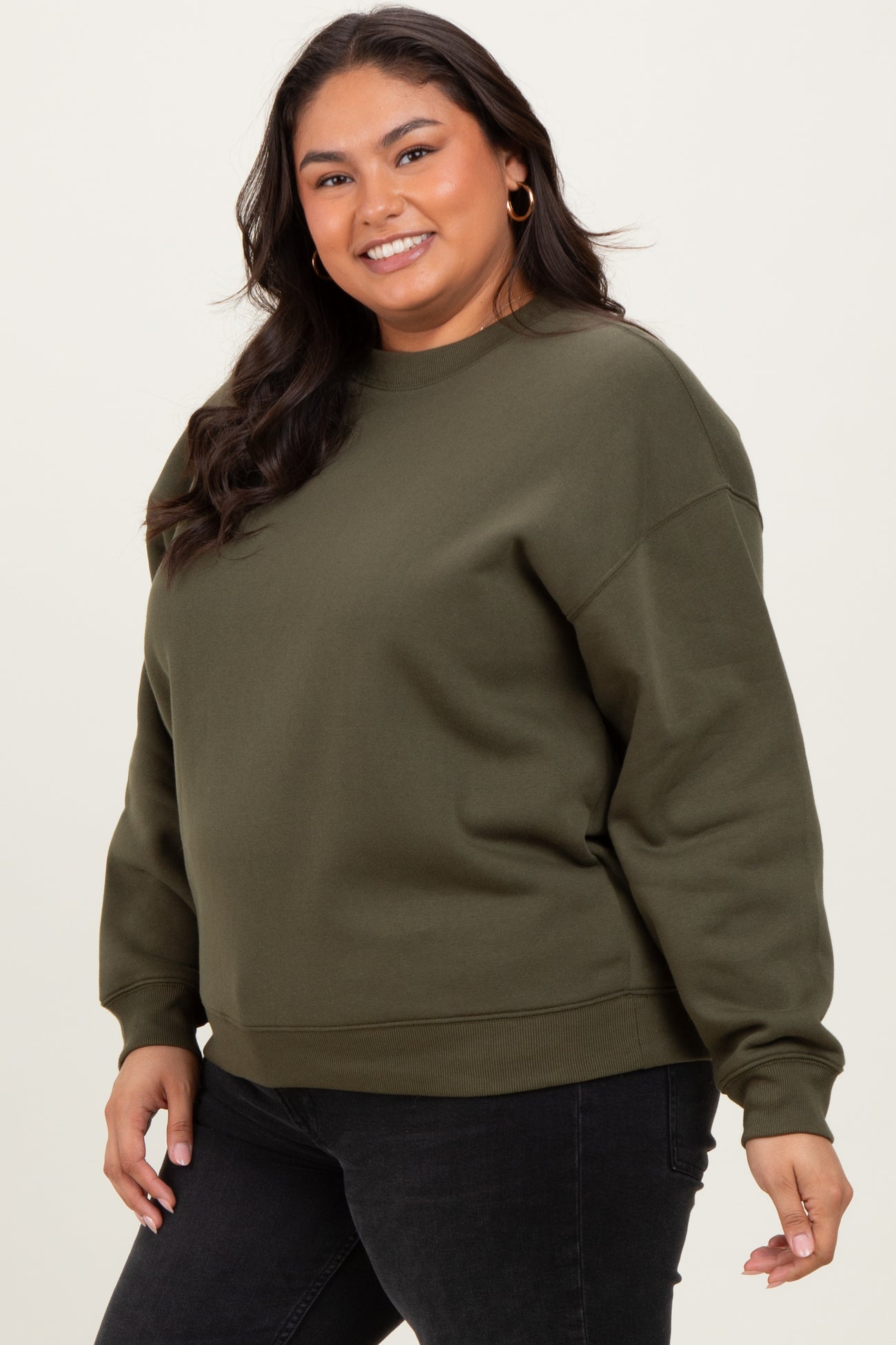 woman wearing an olive green plus size sweatshirt with a relaxed fit and long sleeves, smiling at the camera