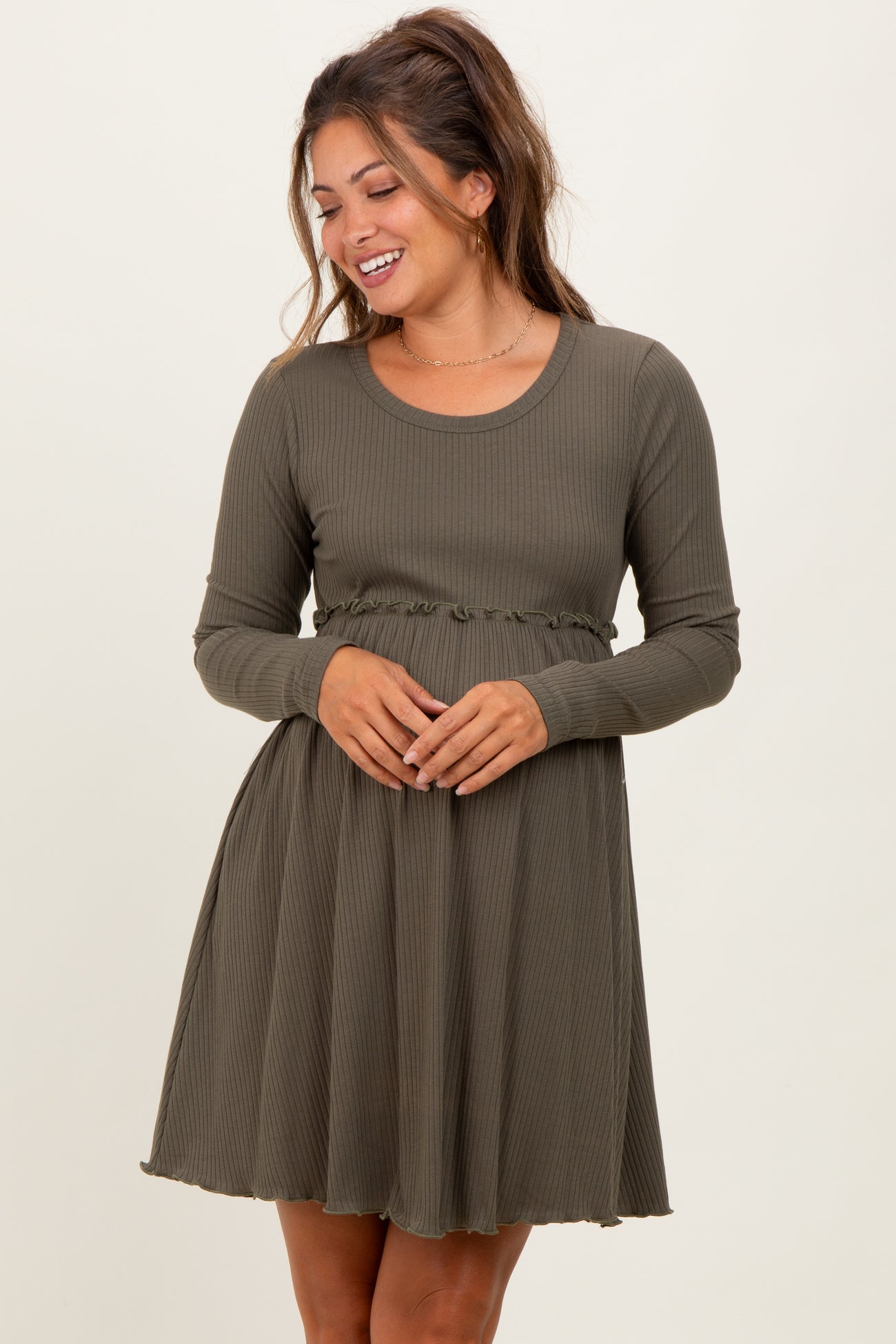 woman wearing a dark green long sleeve maternity dress with a ruffled waistband and a flared skirt