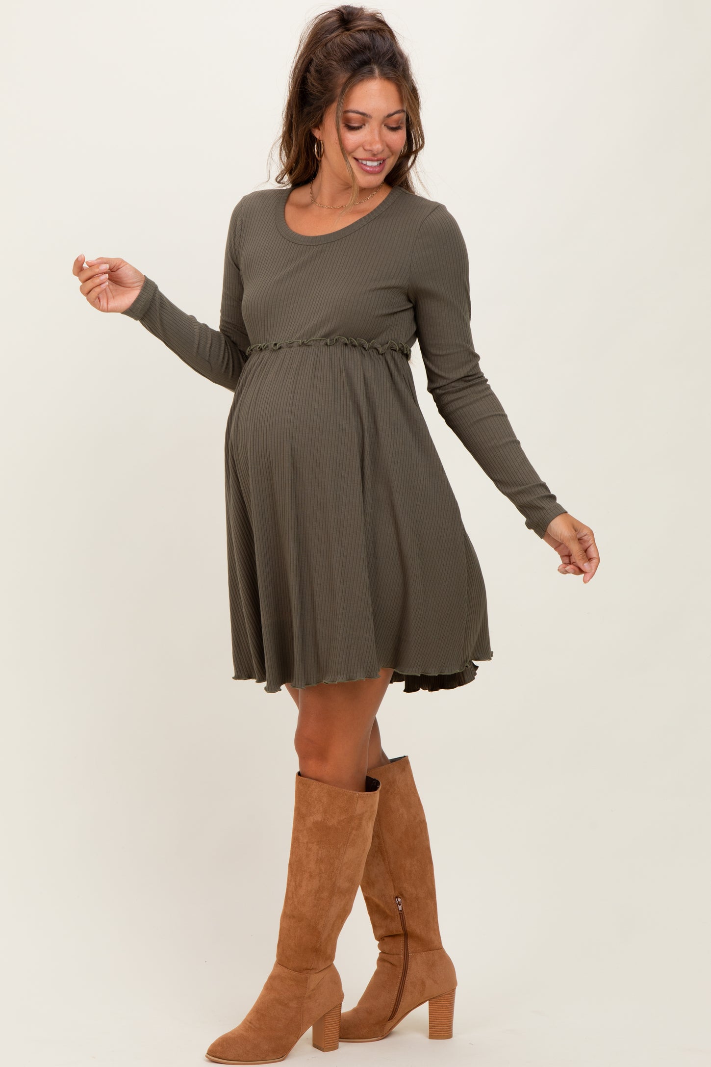woman wearing an olive green long sleeve maternity dress with a ruffled hem and a visible baby bump