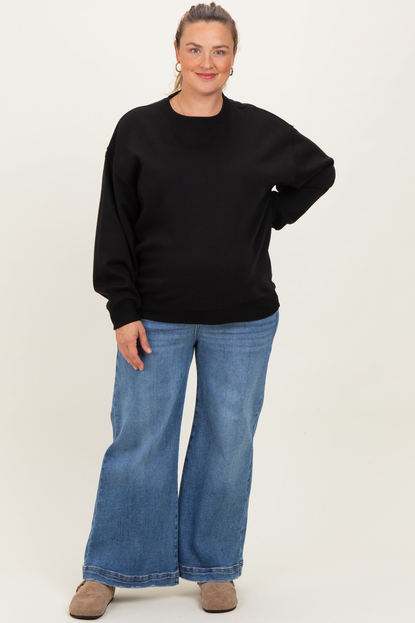 woman wearing a black oversized sweatshirt and wide-leg light blue jeans, with a visible baby bump, maternity plus wear