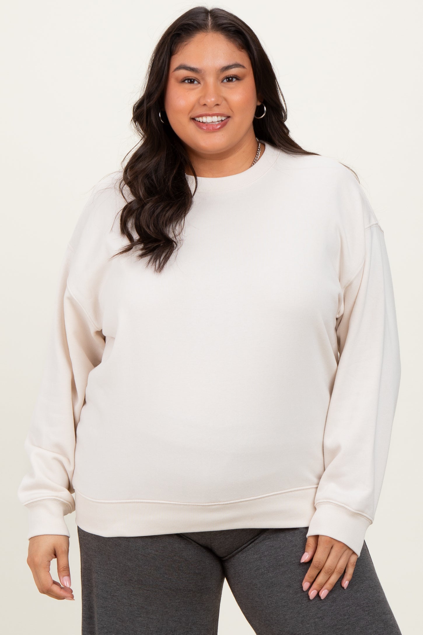 woman wearing a light beige plus size sweatshirt with long sleeves and a relaxed fit, paired with dark gray bottoms