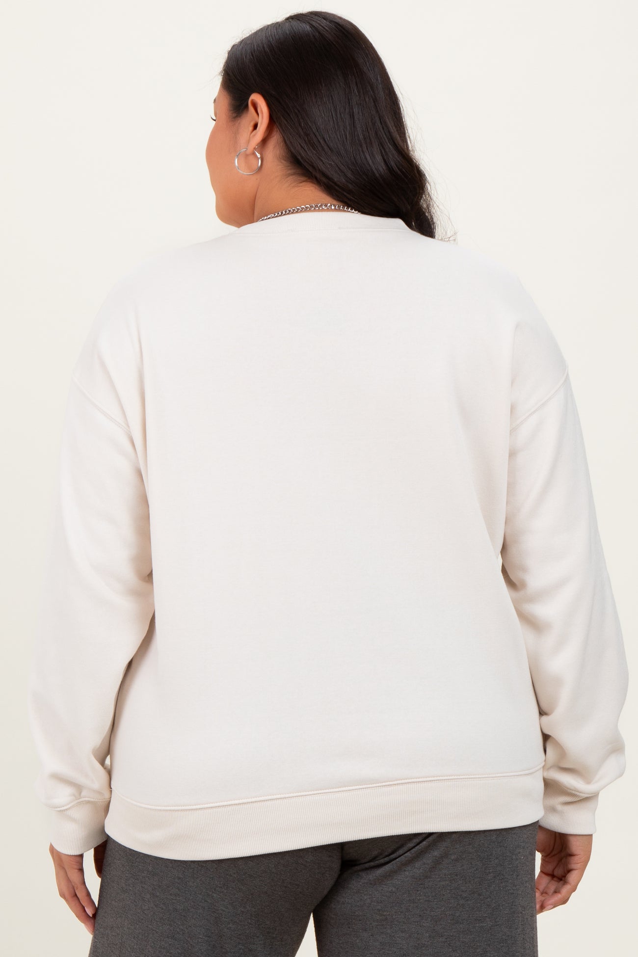 woman wearing a light beige plus size crewneck sweatshirt, seen from the back, with a relaxed fit and long sleeves