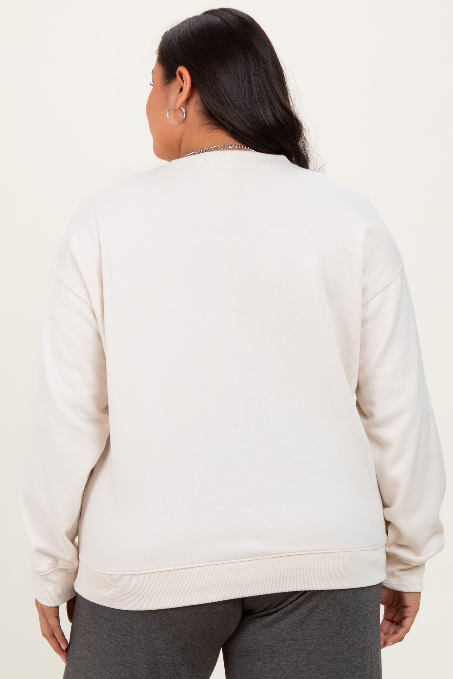 woman wearing a light beige plus size crewneck sweatshirt, seen from the back, with a relaxed fit and long sleeves