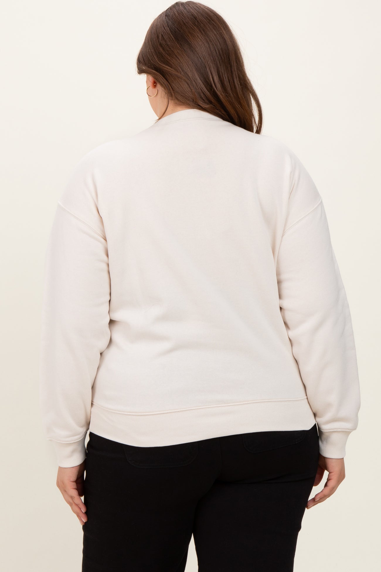woman wearing a light beige maternity sweatshirt, seen from the back, with relaxed fit and cuffed sleeves