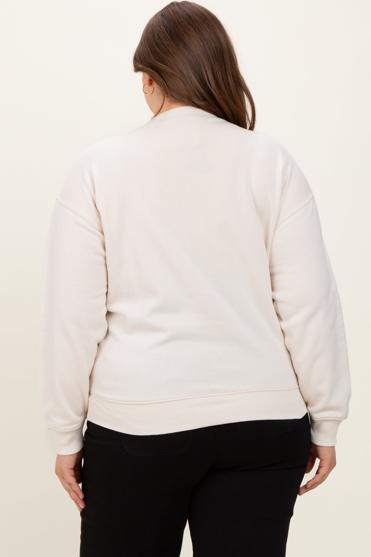 woman wearing a light beige maternity sweatshirt, seen from the back, with relaxed fit and cuffed sleeves