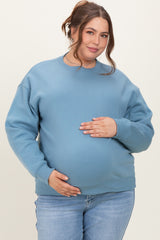 woman wearing a blue maternity sweatshirt, holding her baby bump, paired with light denim jeans