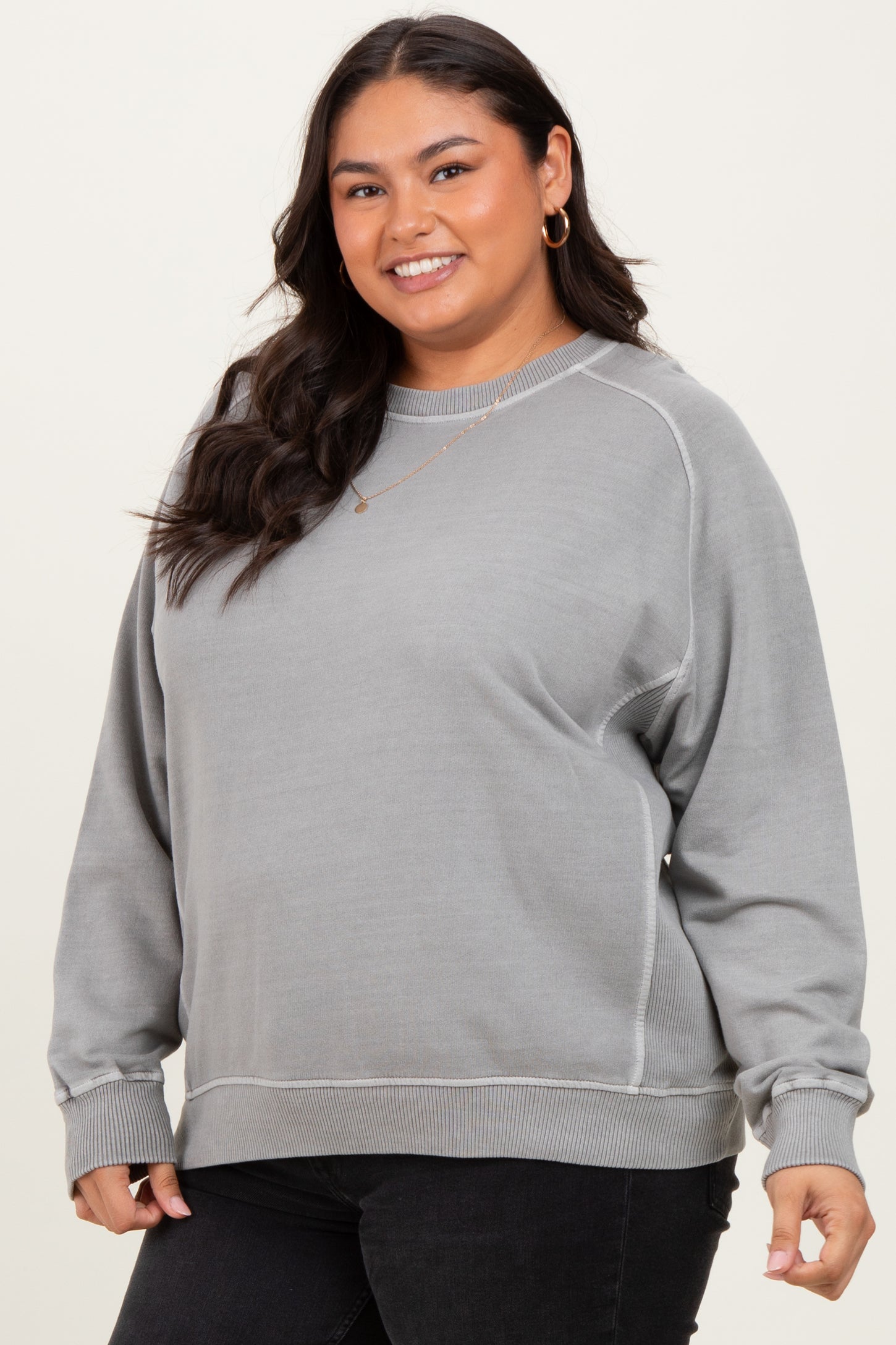 woman wearing a gray plus size sweatshirt with ribbed trim and relaxed fit, smiling at the camera