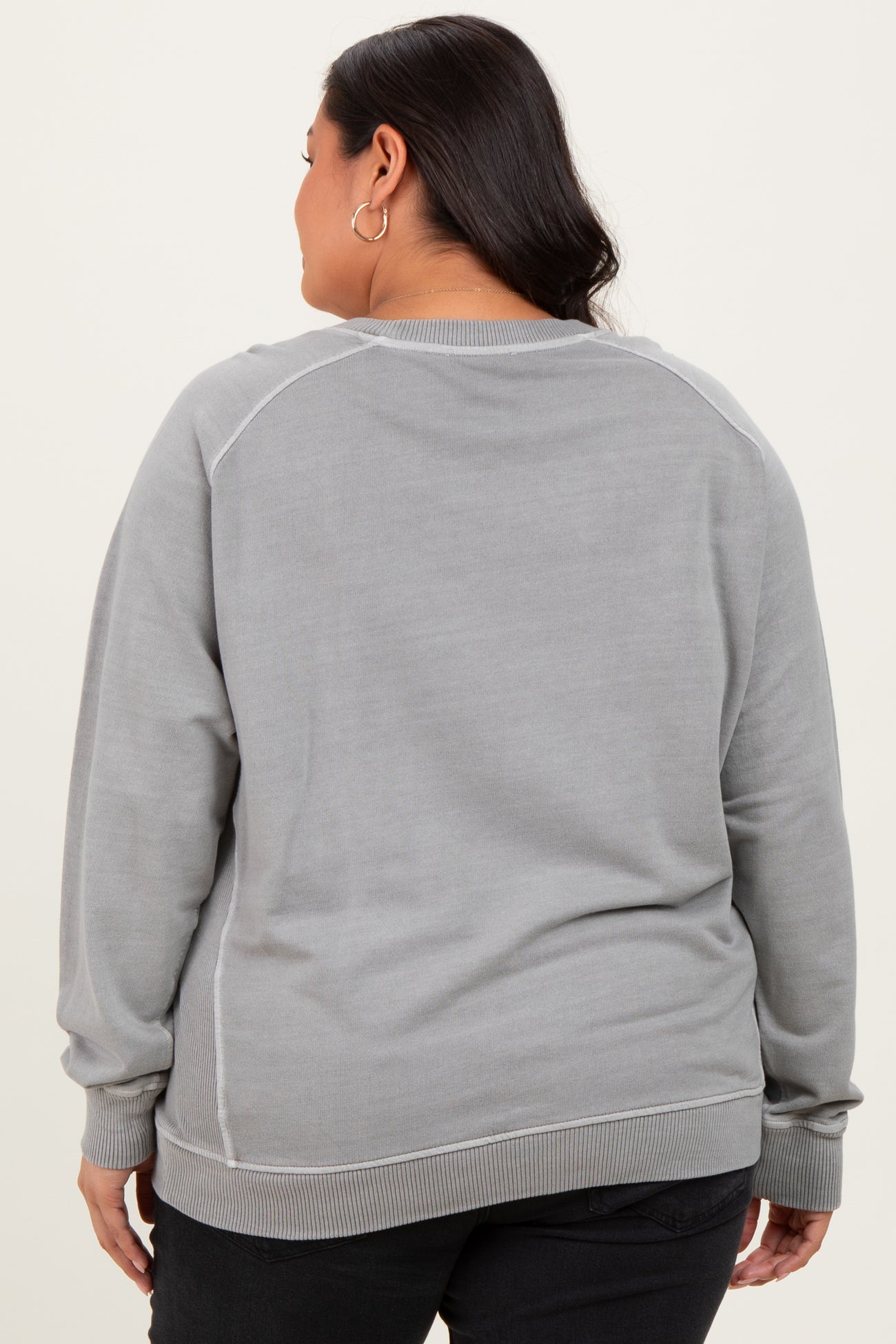 woman wearing a grey long sleeve plus size sweatshirt with a crew neck and ribbed hem, seen from the back
