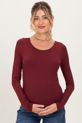 woman wearing a burgundy long sleeve maternity top and holding her baby bump