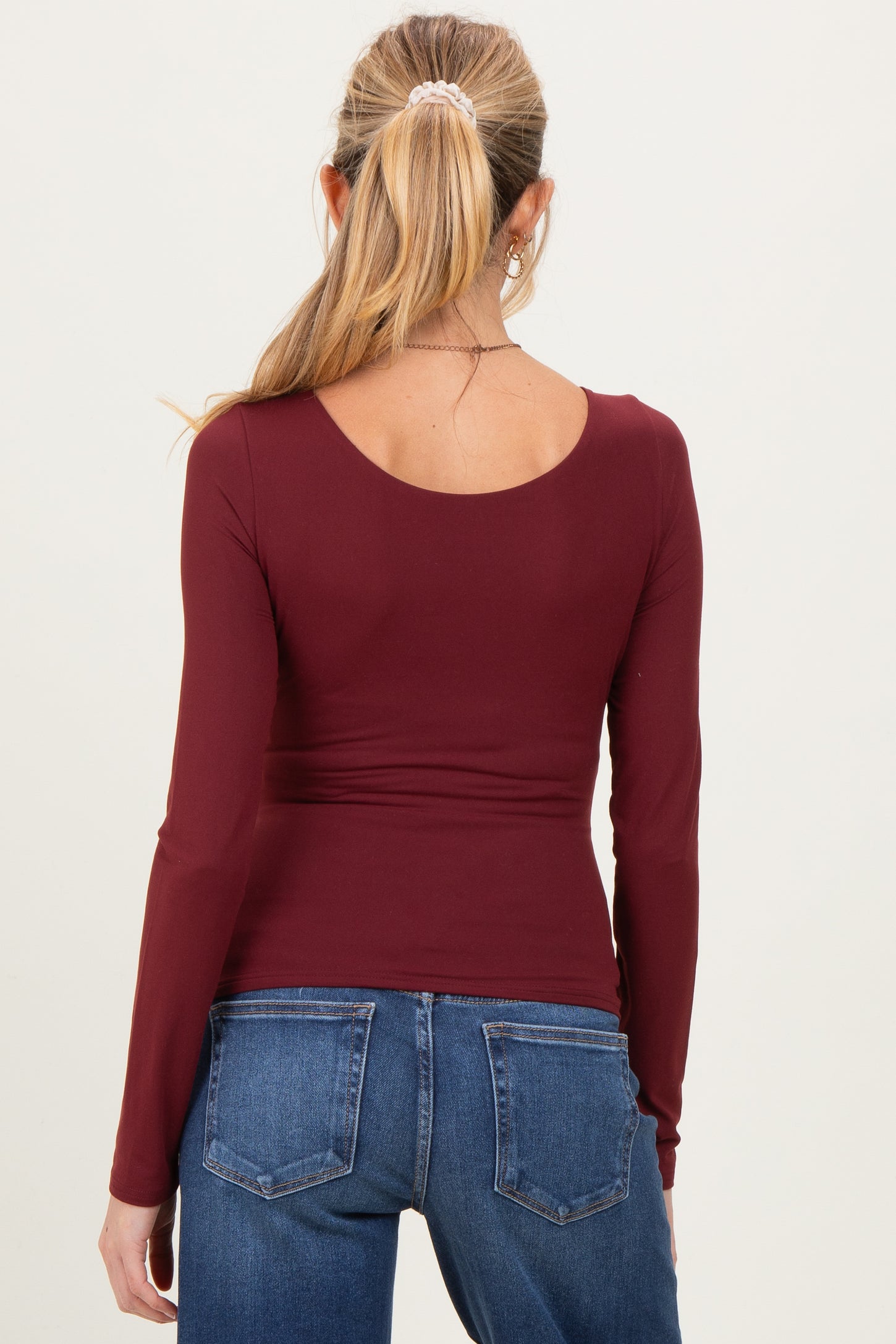 woman wearing a maroon long sleeve maternity top viewed from the back with fitted design and curved hem